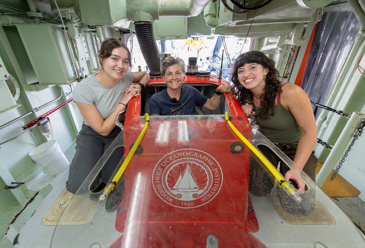 Two students and a faculty member smile at the camera aboard a research vessel 