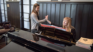 A student and professor sitting at a grand piano high five