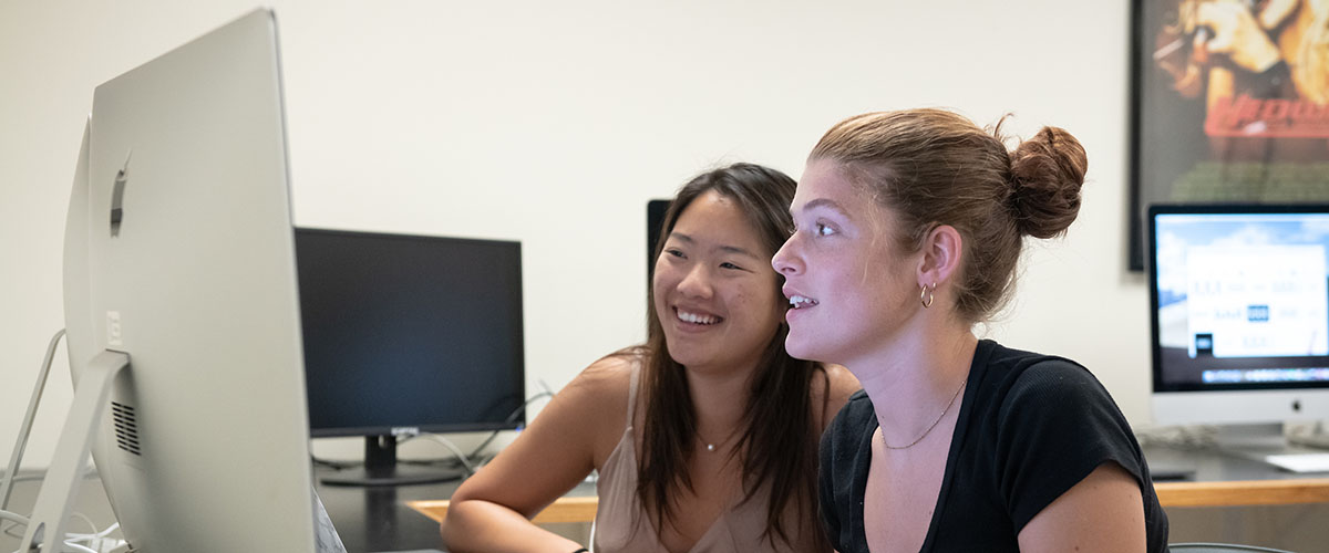 Two students sit at an iMac in a MAC classroom