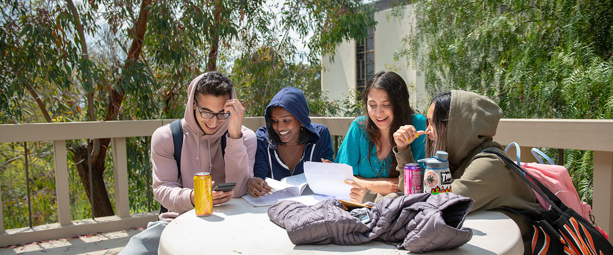 Four students sitting at a table together in front of the Oxy library