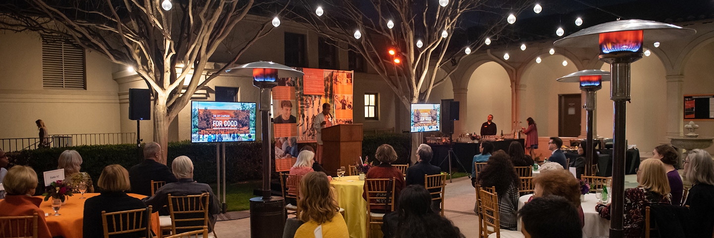 Donors sit at tables for an outdoor Campaign event with lights shining overhead