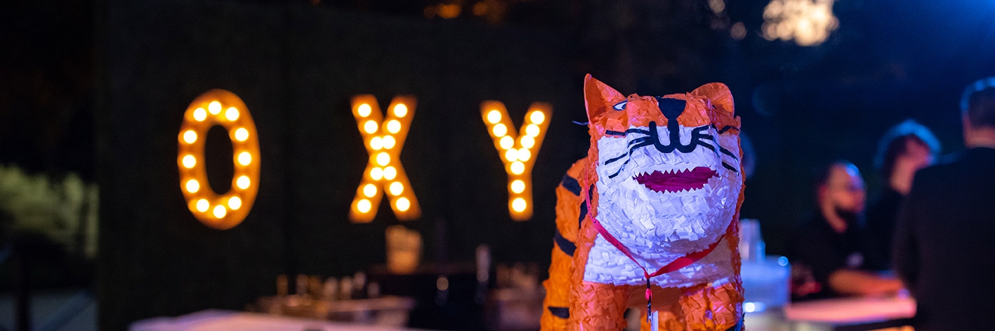 An Oswald the Tiger pinata in front of a sign made of light bulbs that reads "Oxy"